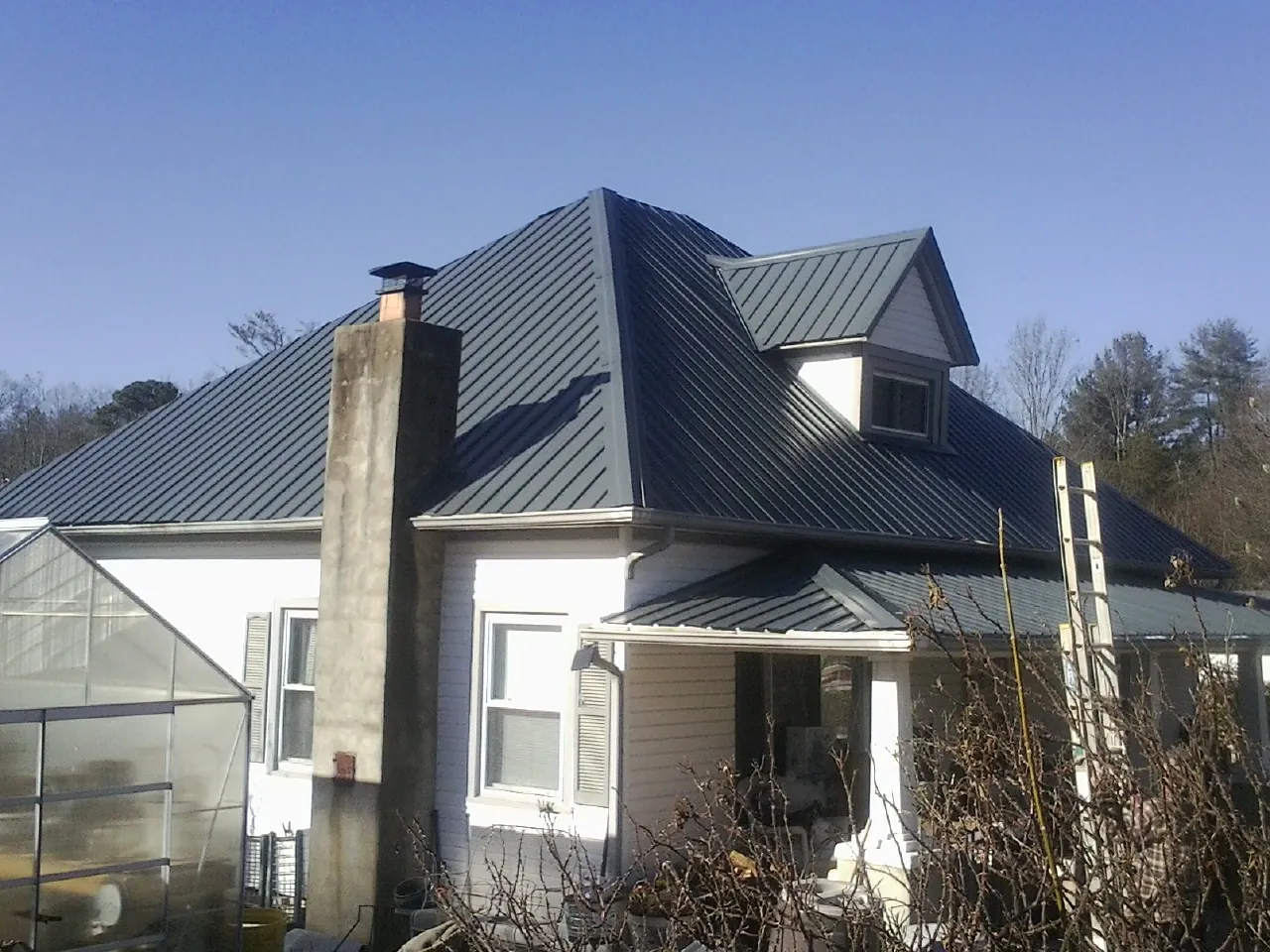 Dark blue standing seam metal roof on a white farmhouse with dormer — Slate & Tile Roof Repair by Roofing Brothers in Rhododendron