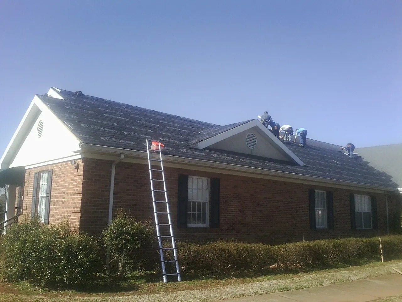 Crew tearing shingles off a brick ranch roof with a ladder set — Emergency Roof Repair work by our crew in Rhododendron