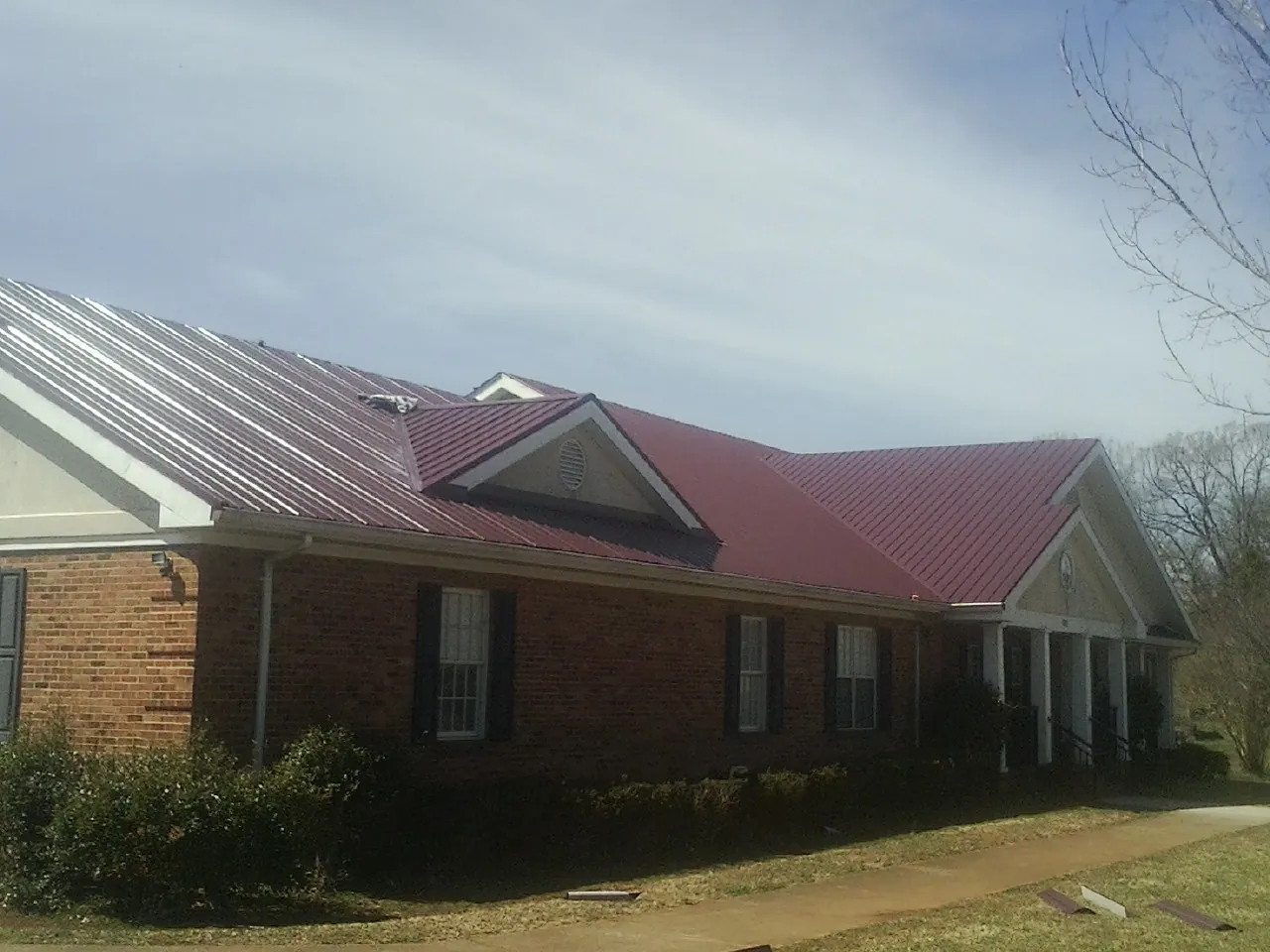 Red metal roof with gabled entries on a long brick building, from a Hail Damage Roof Repair job in Rhododendron