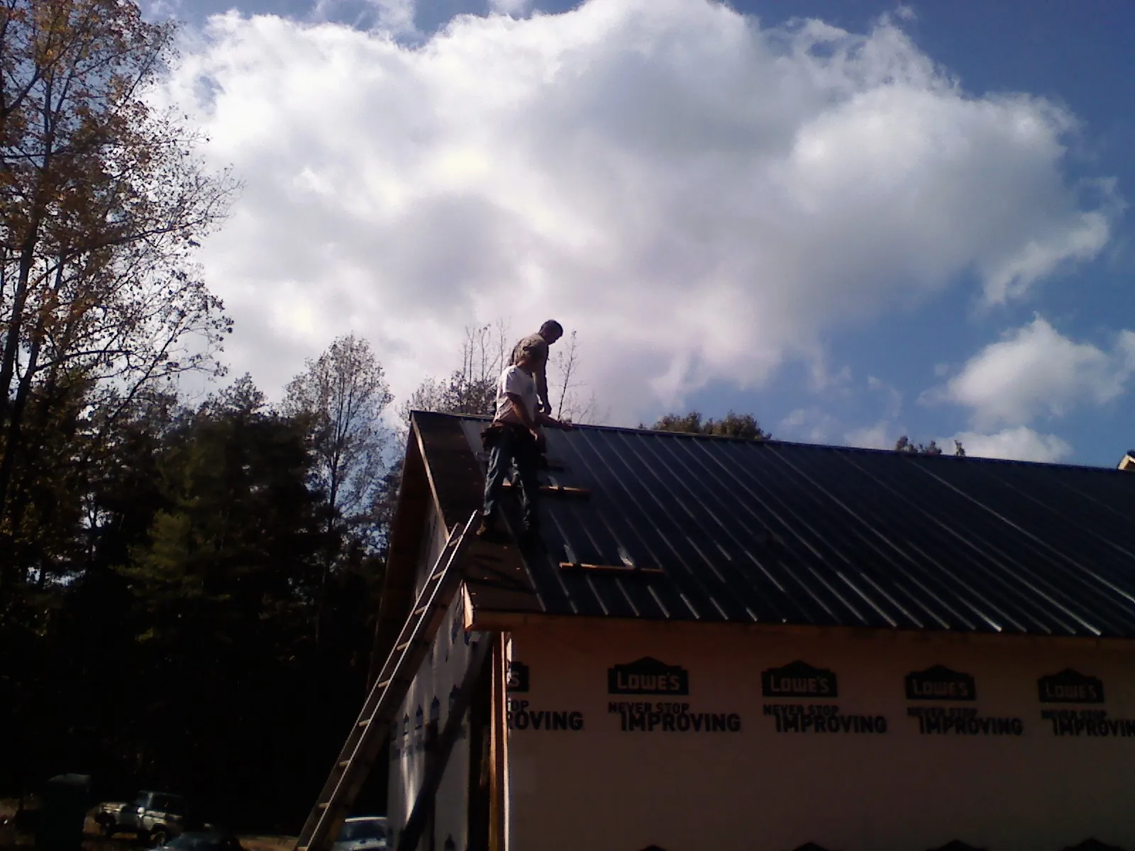 Roofer fastening dark metal panels high against a cloudy sky, from a Roof Inspection job in Rhododendron