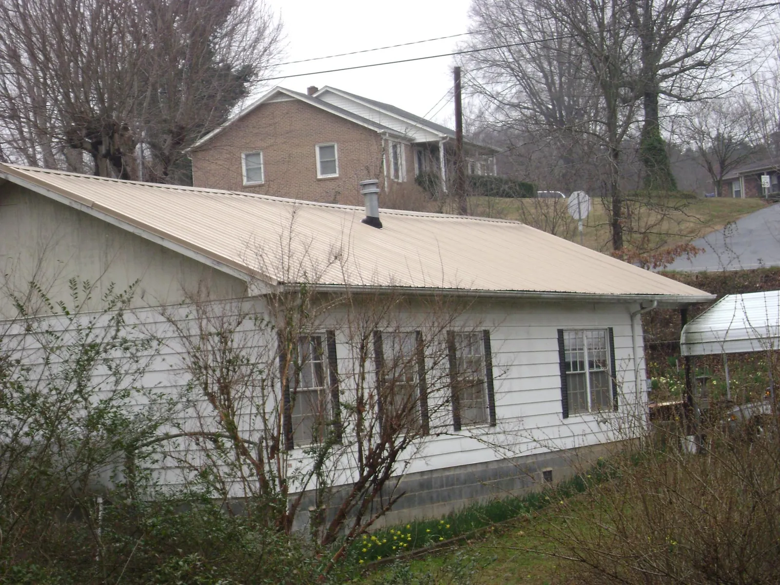 Tan metal roof on a white sided house set into a hillside — Commercial Roofing by Roofing Brothers in Rhododendron